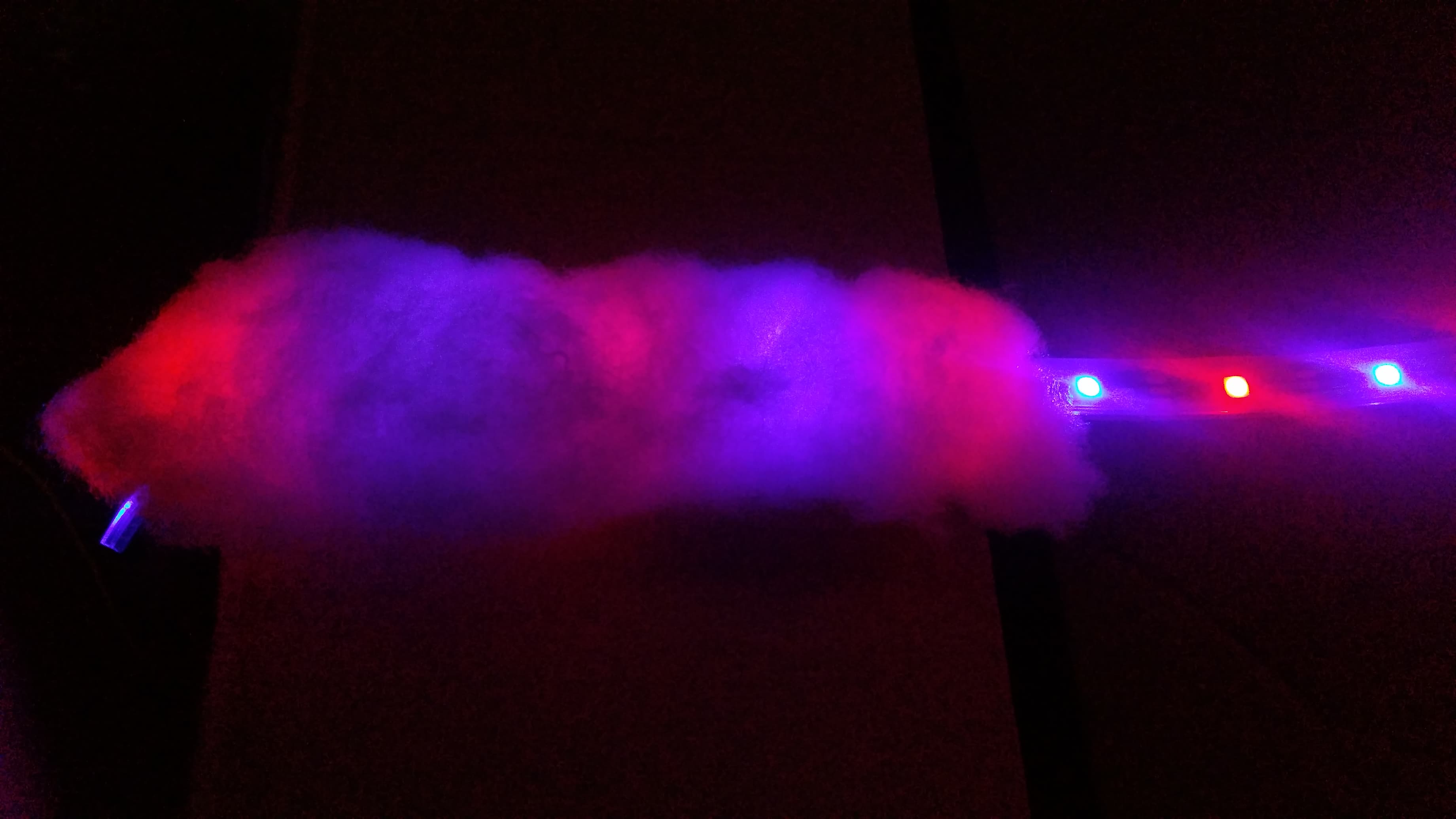 An LED light strip illuminating a handful of fiberfill material with purple and red. With the lights off